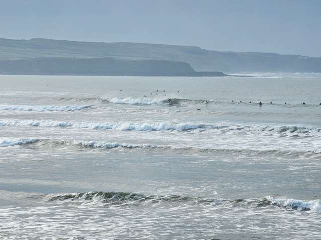 Surfer riding a head high clean wave on Cornish point as many more sit outside